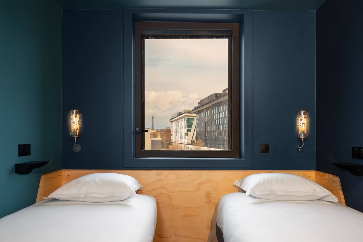 Ein Zimmer mit zwei Betten, einem großen Fenster und Stadtblick sowie Wandleuchten.