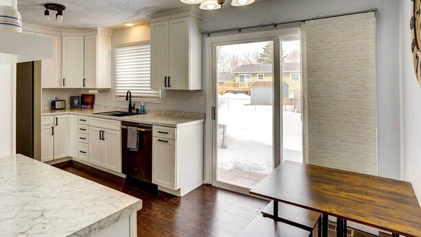A modern kitchen with white cabinets, a marble countertop, and a wooden dining table. - Cozy Sioux Falls Home - 7 Mi to Downtown! (Sioux Falls)