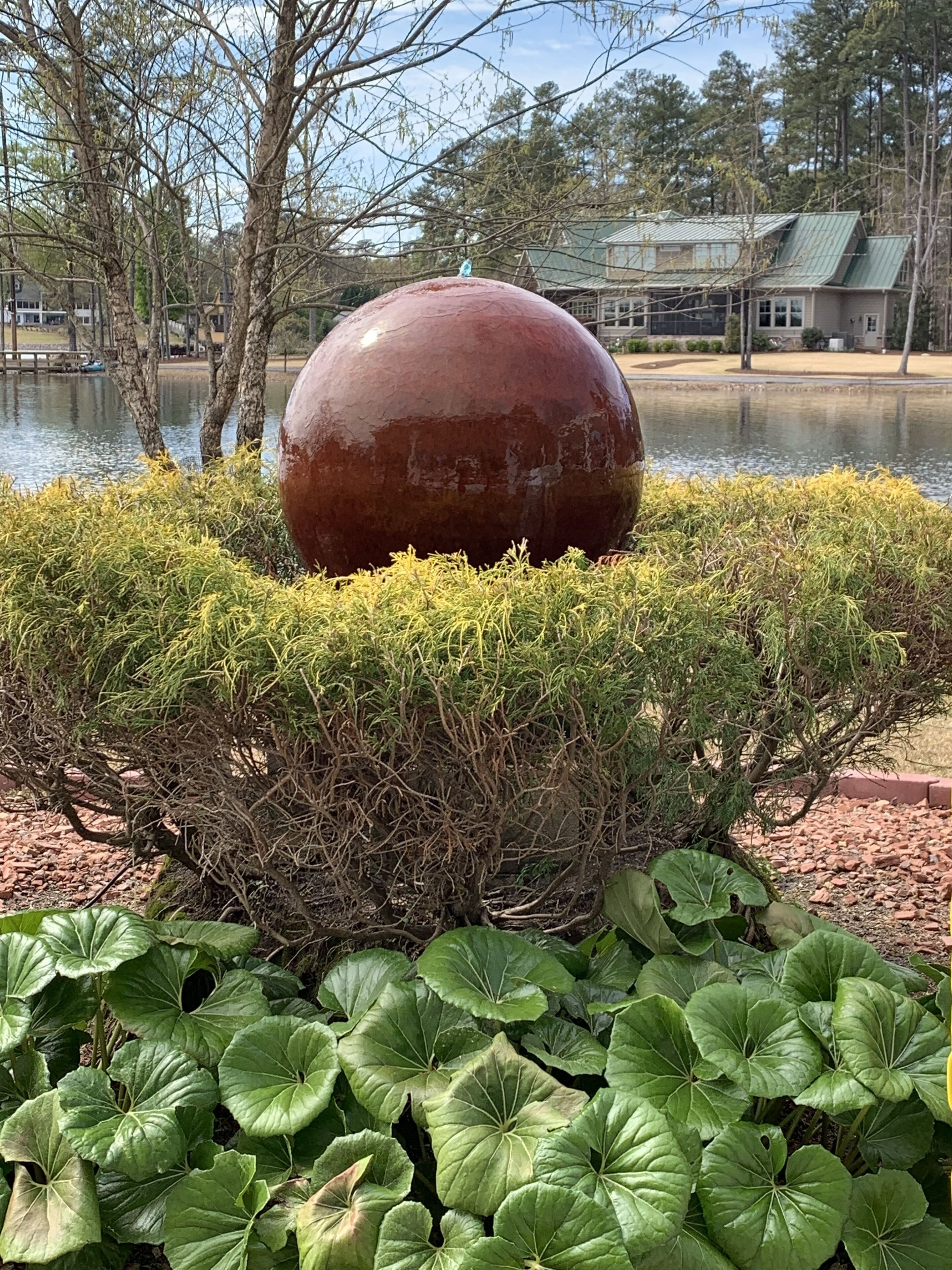 Une grande sculpture sphérique, entourée d’une haie bien entretenue et d’une végétation luxuriante.