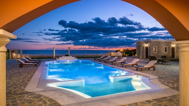Ein Poolbereich mit Liegestühlen und Blick auf das Meer im Abenddämmerung.