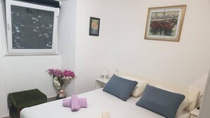 A neatly made bed with pillows and towels, a small bedside table with a lamp, a window with a view, and a framed picture on the wall. - Iva - Modern Downtown - A2 Navada (Split)