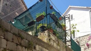 A stone wall with a wooden door, a green metal structure above, and a building in the background. - Iva - Modern Downtown - A2 Navada (Split)