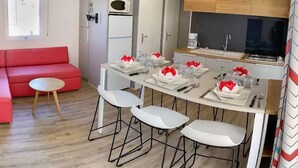 Una cocina moderna con electrodomésticos blancos, un comedor con sillas blancas, un sofá rojo y una pequeña mesa redonda.