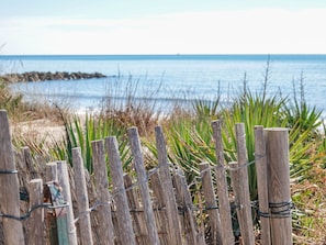 A wooden fence with barbed wire, leading to a beach with green vegetation and a clear view of the ocean. - Camping Pleine Mer (Vias)