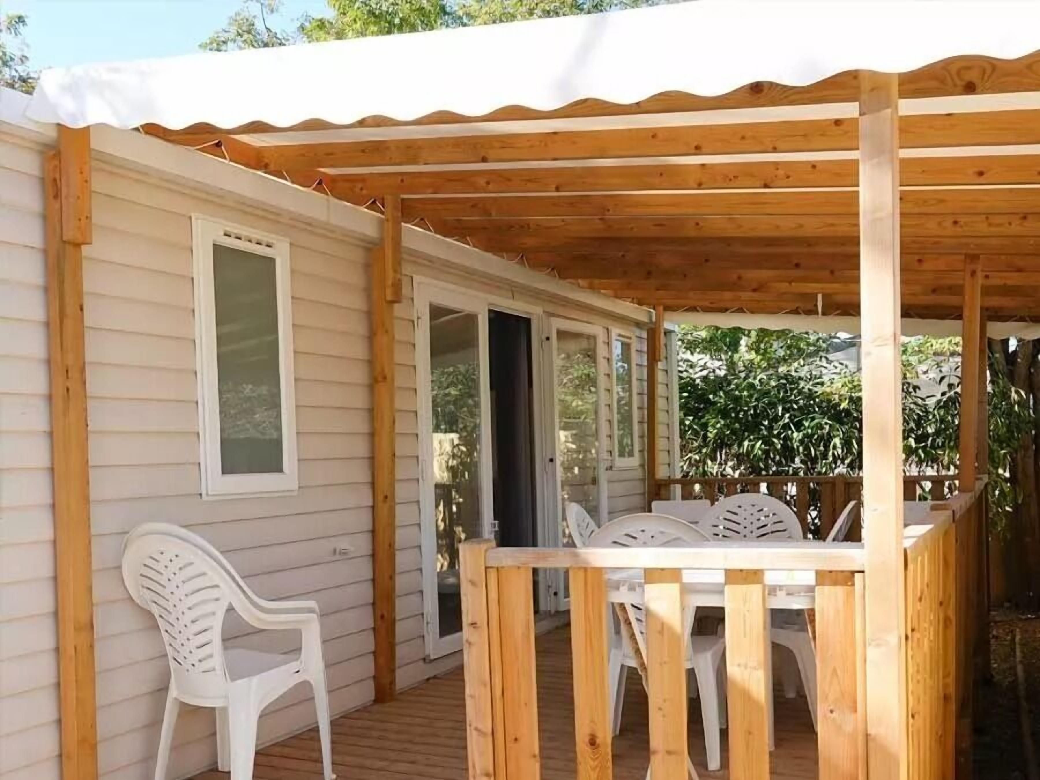 Un espace extérieur abrité, doté d’une terrasse en bois, d’une chaise en plastique blanche et d’une table avec des chaises.