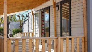 Un espacio al aire libre cubierto con mobiliario de madera y un ventanal corredero que da a una habitación.