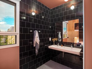 A modern bathroom with black tiles, a white sink, and a mirror.