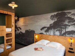 A bedroom with a bed, a wooden headboard, a mural of trees, and two wall-mounted lights.