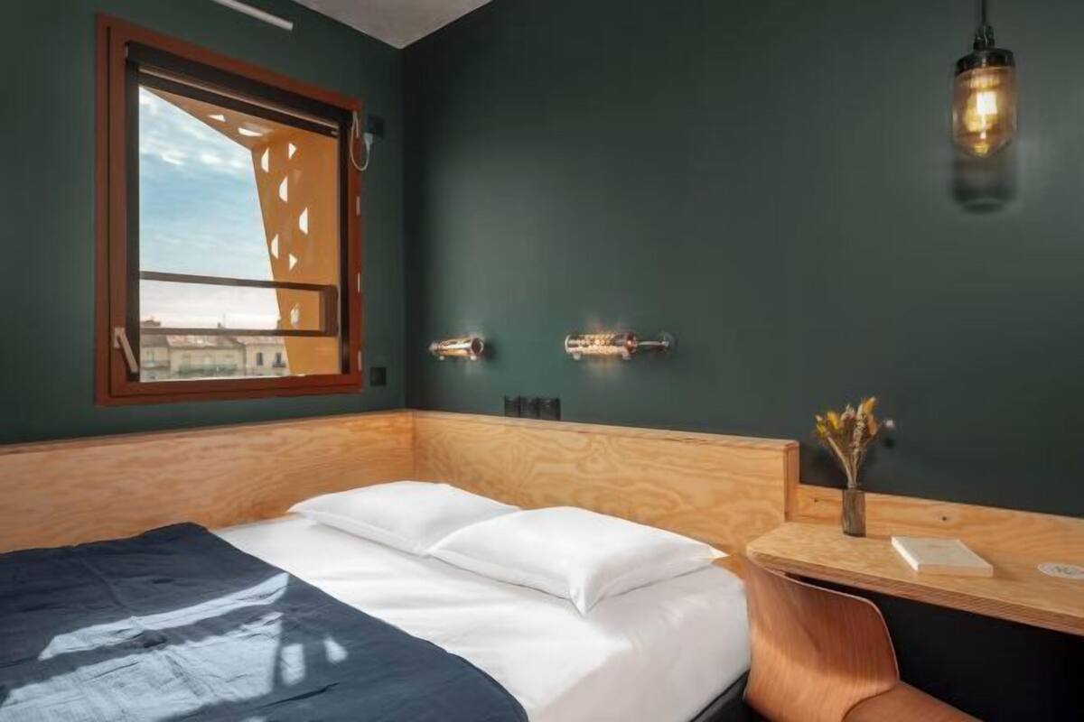 A room with a bed, a window, a desk, and a hanging light fixture.