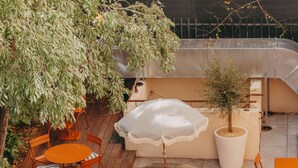 An outdoor patio with multiple tables and chairs, some with umbrellas, surrounded by greenery and potted plants. - Eklo Hotels Montpellier City center Saint-Roch train station (Montpellier)