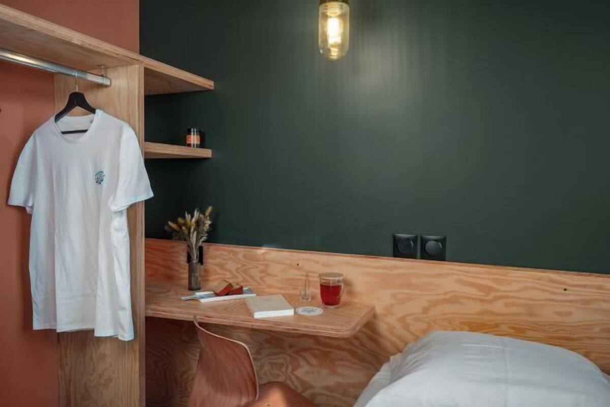A room with a wooden desk, a hanging white t-shirt, a small plant, and a wall-mounted light fixture.