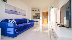 Ein modernes Wohnzimmer mit einem blauen Sofa, einem Flachbildfernseher und einer Küche im Hintergrund.