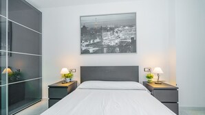 Ein modernes Schlafzimmer mit einem großen Bett, zwei Nachttischen mit Lampen, einem Stadtbild an der Wand und einer Schiebetür aus Glas.