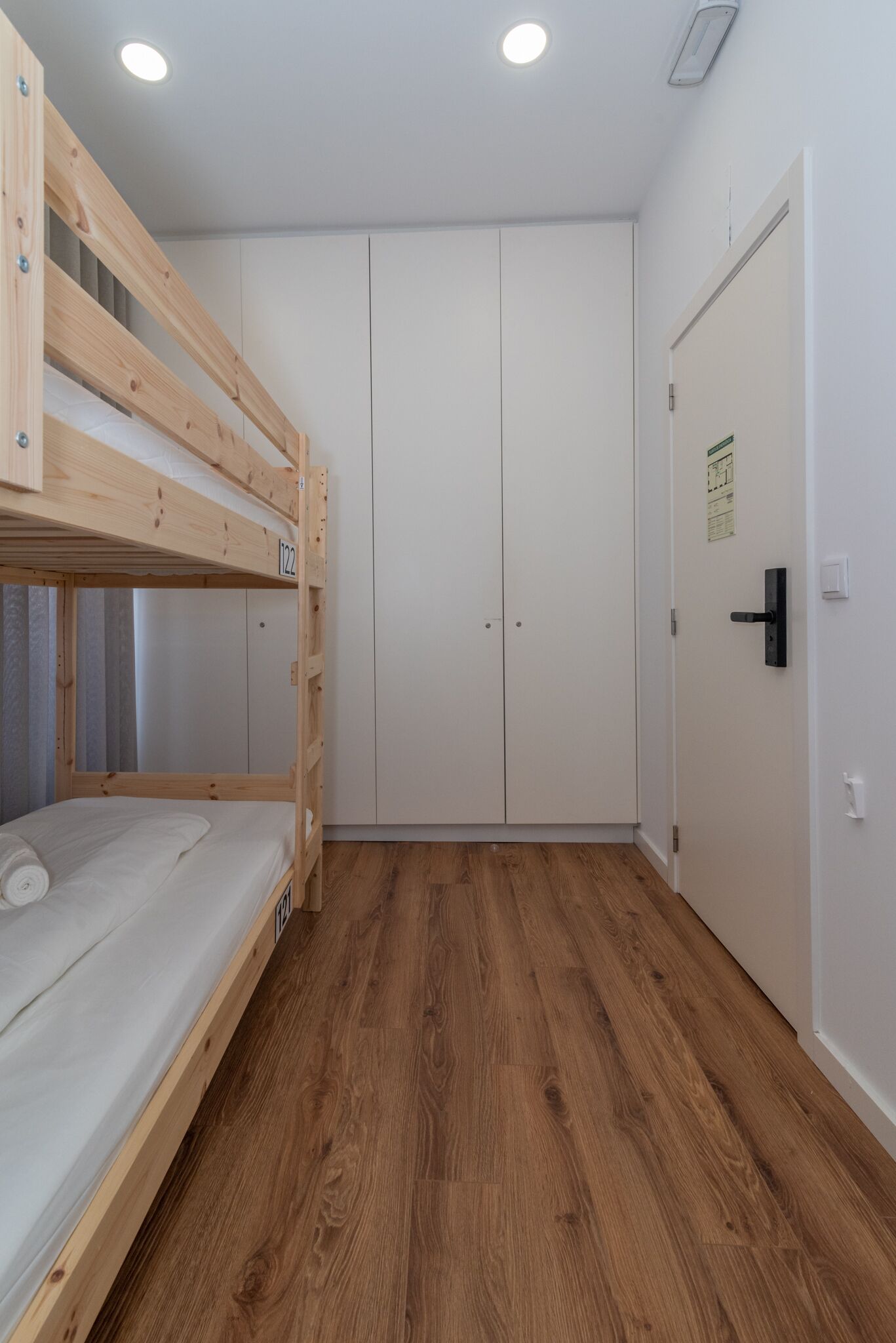 A room with a bunk bed, white wardrobe, and a door with a handle.