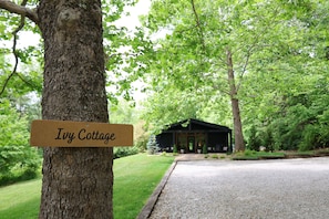 Un cartel en un árbol que dice 'Ivy Cottage', con un camino de grava que lleva a un edificio rodeado de follaje.