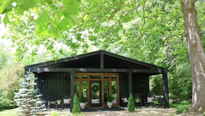 A covered outdoor seating area with a wooden structure, potted plants, and a gravel pathway.