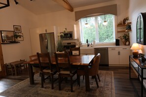 A modern kitchen with a dining area, wooden furniture, and a window with a view of greenery. - Ivy Cottage by Creative Cabins (Logan)
