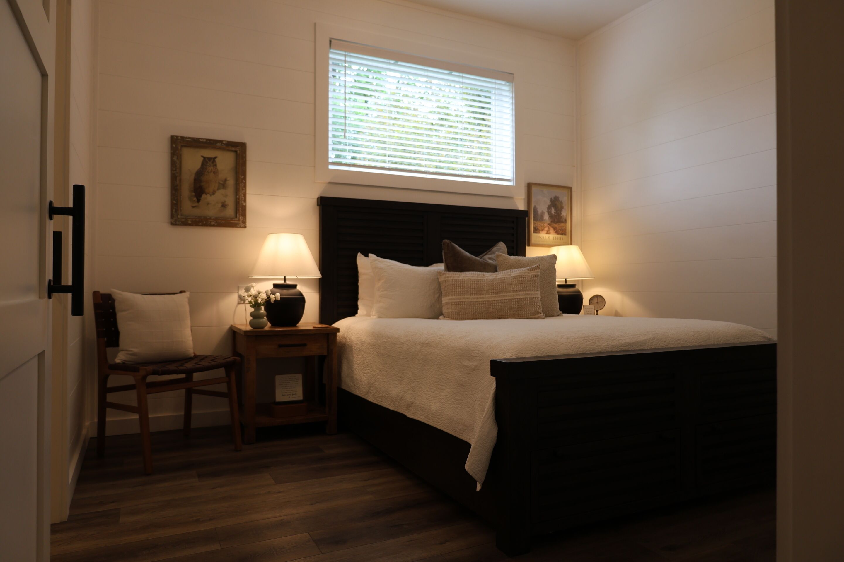 A bedroom with a bed, two bedside tables with lamps, a chair, and a window with blinds.