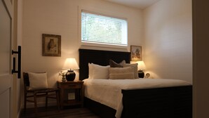 A bedroom with a bed, two bedside tables with lamps, a chair, and a window with blinds.