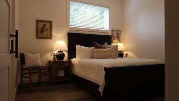 A bedroom with a bed, two bedside tables with lamps, a chair, and a window with blinds.
