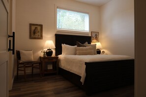 A bedroom with a bed, two bedside tables with lamps, a chair, and a window with blinds.
