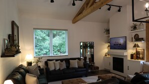 A living room with a fireplace, a television, and a large window with blinds.