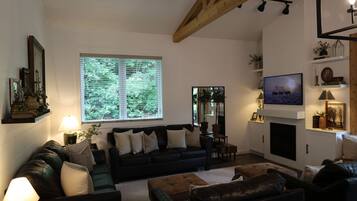 A living room with a fireplace, a television, and a large window with blinds.