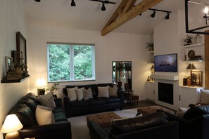 Un salón con chimenea, televisor y un amplio ventanal con persianas.
