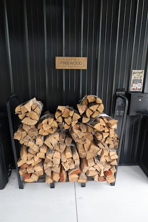 A stack of firewood labeled 'FIREWOOD' in front of a black metal wall.