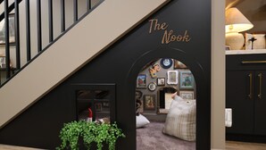 Una scala con un arco nero con l'insegna ‘The Nook’, che conduce a un angolo accogliente per la lettura, con un divano e delle librerie.