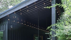 Zona relax all'aperto coperta, con sedie e barbecue, circondata da un patio in ghiaia e vegetazione.