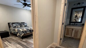A bedroom with a bed, wooden flooring, a ceiling fan, and a view into the bathroom. - SPORTSMAN'S PARADISE (Helena)