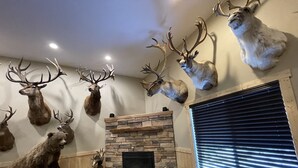 A room with a stone fireplace, mounted animal heads, and a window with blinds. - SPORTSMAN'S PARADISE (Helena)