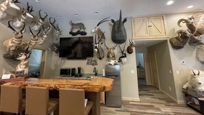 A modern kitchen with a wooden dining table, a flat-screen TV mounted above it, and various animal skulls and antlers decorating the walls. - SPORTSMAN'S PARADISE (Helena)