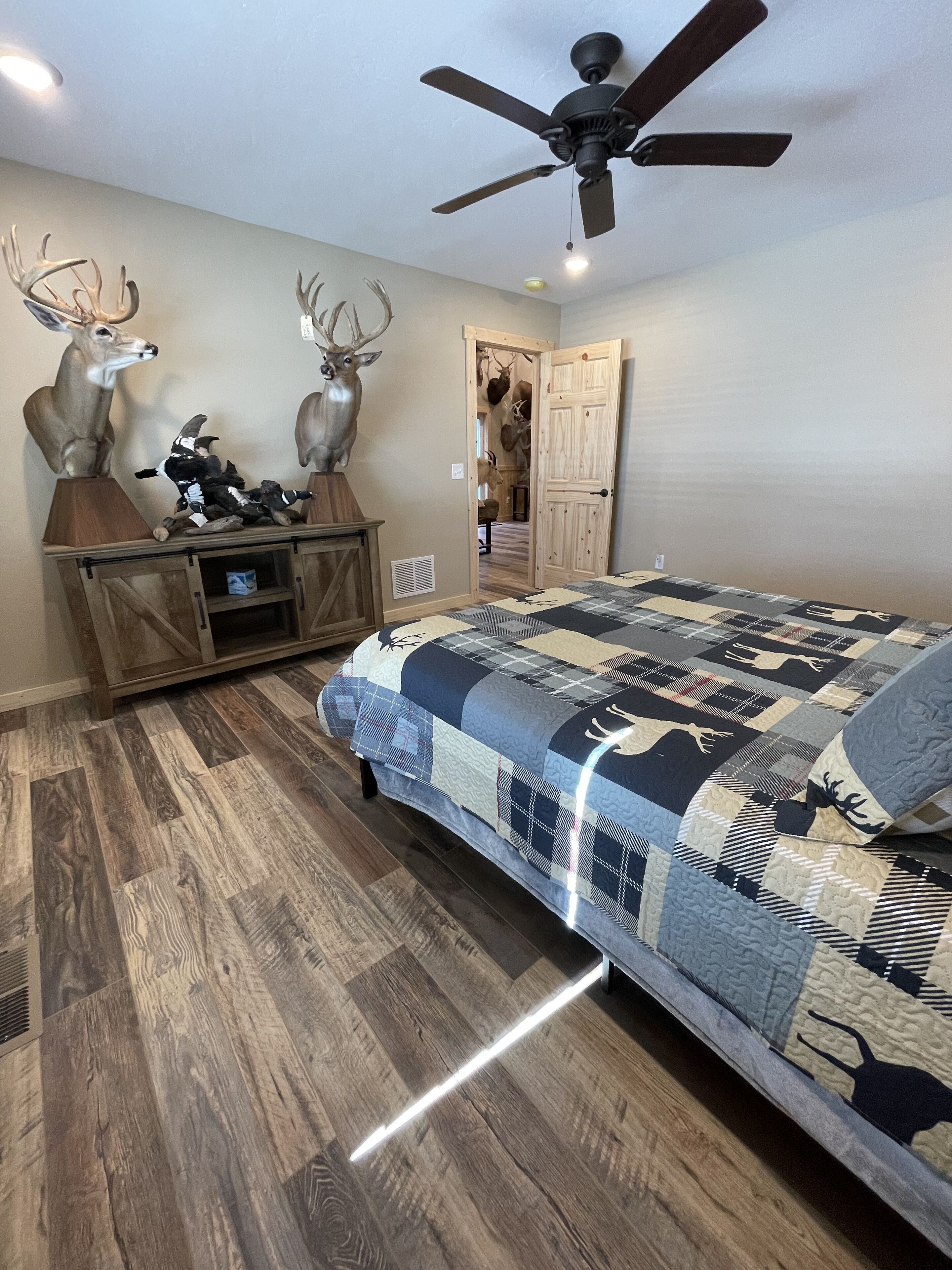 Een slaapkamer met een bed, houten vloer, plafondventilator en rendierhoorns op een kast.