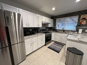 A modern kitchen with white cabinets, stainless steel appliances, a black countertop, and a window with blinds. - Hidden Gem in Quiet Neighborhood (West Valley City)