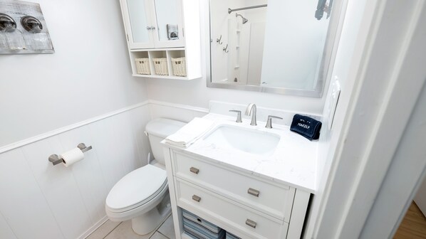 Un baño moderno con inodoro blanco, un lavabo con espejo arriba y zona de ducha.