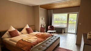 A spacious bedroom with a large bed, a small table, a chair, and a view of the outdoors through a large window. - Hotel Gonzlay (Traben-Trarbach)