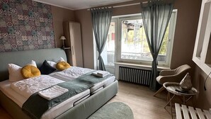 A bedroom with a bed, a desk, a chair, a radiator, and a window with curtains. - Hotel Gonzlay (Traben-Trarbach)