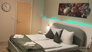 A modern bedroom with a bed, a clock, a door, and a wall-mounted lamp. - Hotel Gonzlay (Traben-Trarbach)