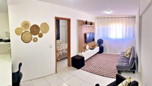 A modern living room with a sofa, a TV, and a coffee table. There is a dining area with a table and chairs.