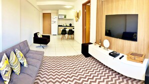 A modern living room with a grey sofa, a TV mounted on a wooden wall, and a dining area in the background.