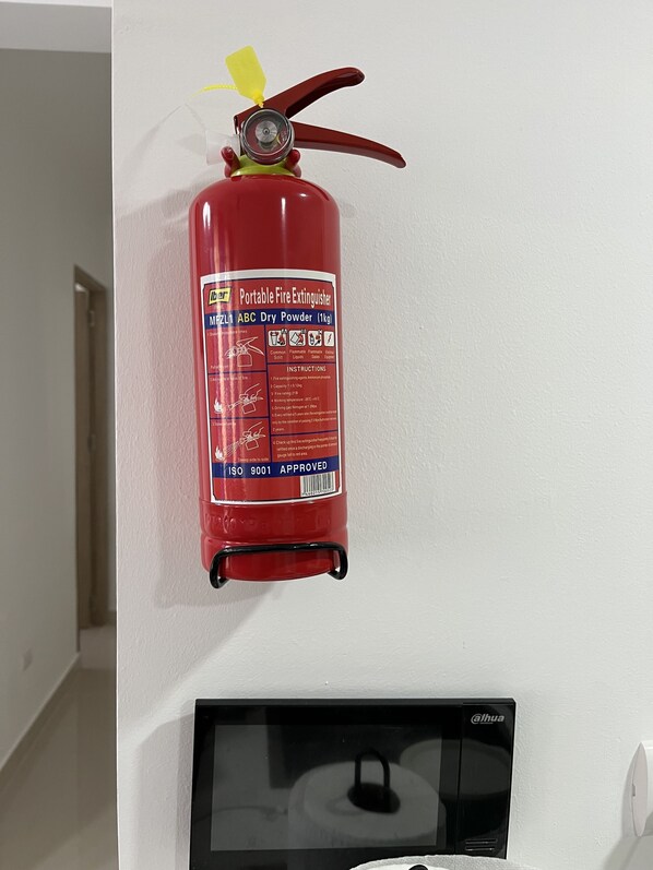 Un extincteur rouge, portatif, fixé sur un mur blanc.