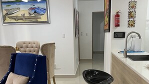 A modern living room with a blue sofa, a black bar stool, and a painting of boats on the wall. - 10Min. Del Aeropuerto apt.picina aire wifi 24H seguridad patio de juegos parqueo (Santiago De Los Caballeros)