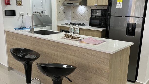 A modern kitchen with a central island, stainless steel appliances, and wooden cabinetry. - 10Min. Del Aeropuerto apt.picina aire wifi 24H seguridad patio de juegos parqueo (Santiago De Los Caballeros)