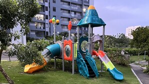 A playground with slides and climbing structures, surrounded by grass and plants, with a building in the background. - 10Min. Del Aeropuerto apt.picina aire wifi 24H seguridad patio de juegos parqueo (Santiago De Los Caballeros)
