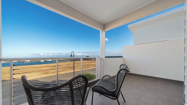 A balcony with two wicker chairs and a table, overlooking a beach with boats and a clear sky. - Sunny Dais Beachfront - stunning views of the Marina, Clifftops and Port Vincent (Port Vincent)