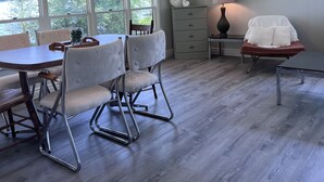A dining area with a wooden table and chairs, a chandelier, and a view of trees through large windows. - Private getaway on Lower Buckhorn Lake (Trent Lakes)