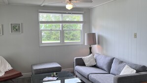 A living room with a gray sofa, a glass coffee table, and a ceiling fan. - Private getaway on Lower Buckhorn Lake (Trent Lakes)