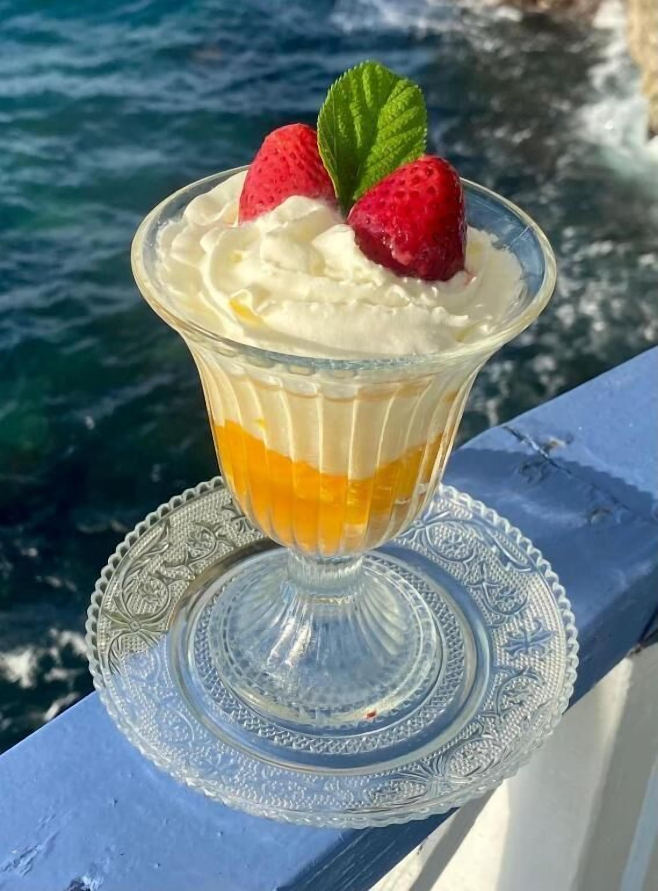 Un dessert servi dans un bol en verre, posé sur une assiette décorative, le tout présenté sur un fond représentant une étendue d’eau.